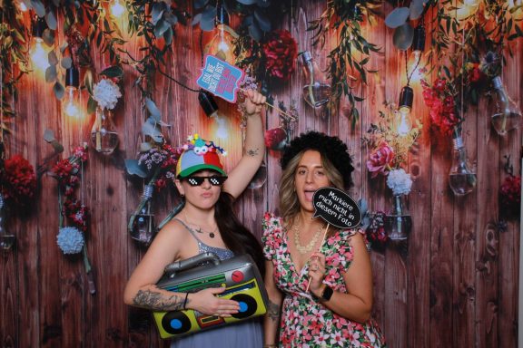 Zwei Frauen mit Accessoires posieren vor der Fotobox und lösen ein Foto aus.